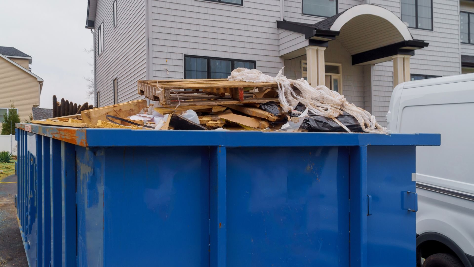 Blue dumpster filled with wood debris and construction waste near residential building