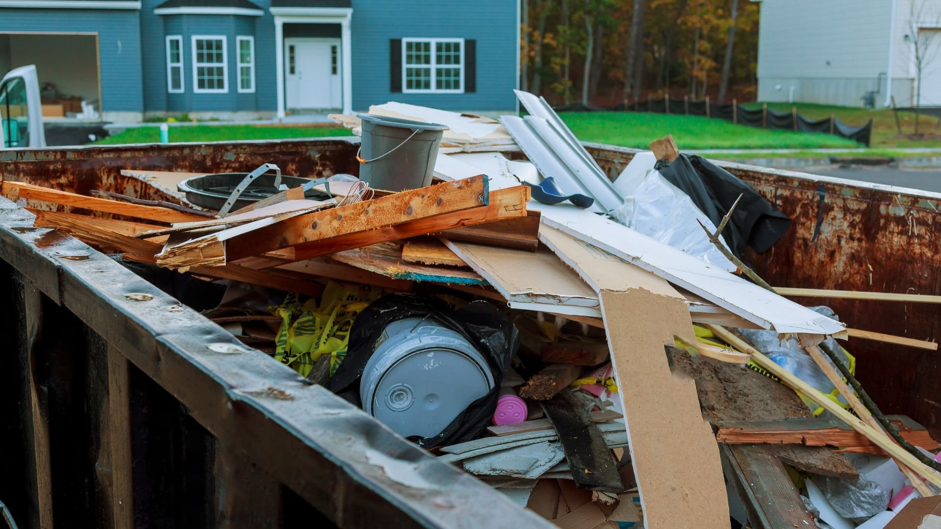 Construction debris in a rusty dumpster with blue house in background