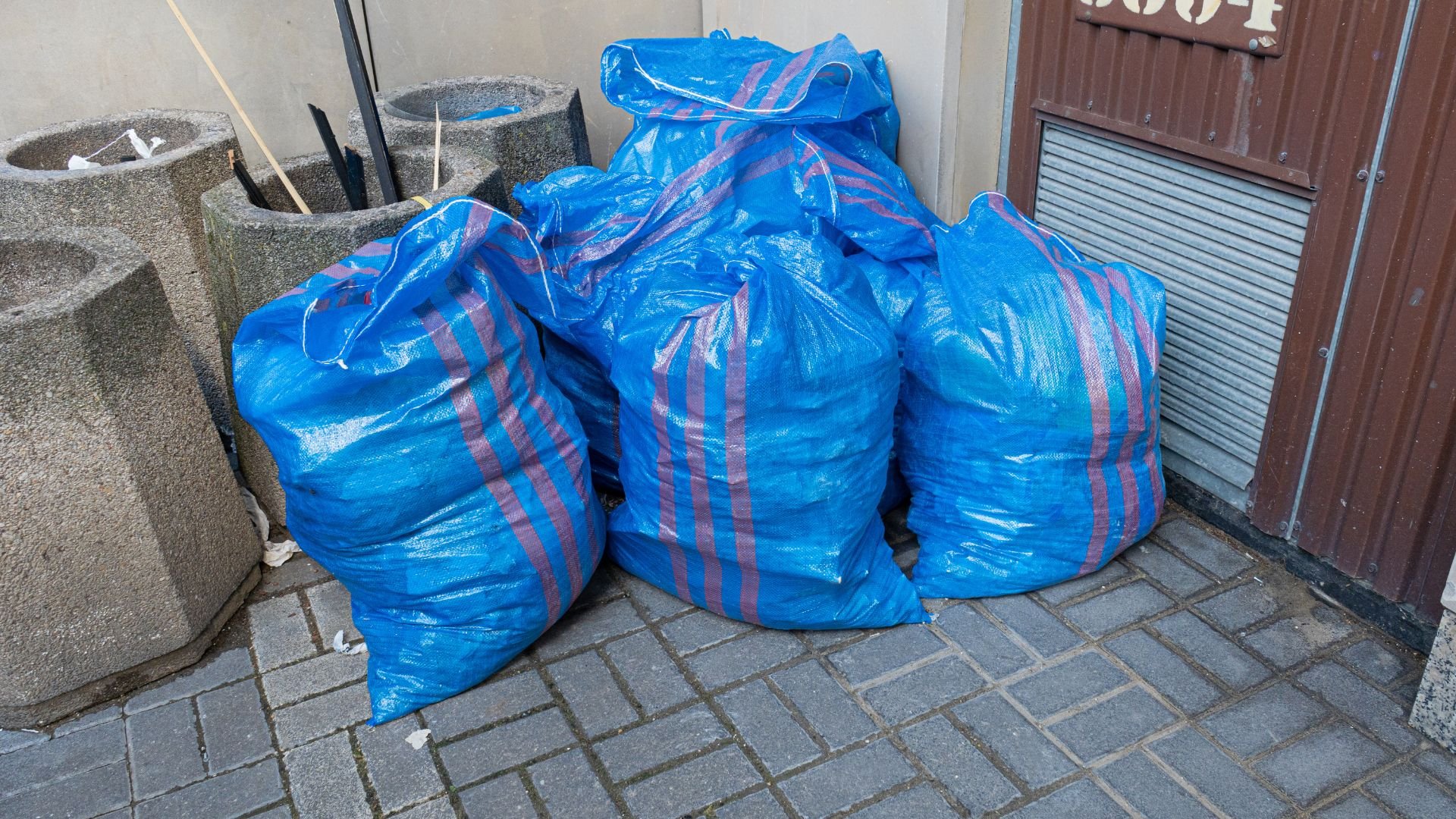 Blue trash bags with pink stripes sitting near concrete planters and wall