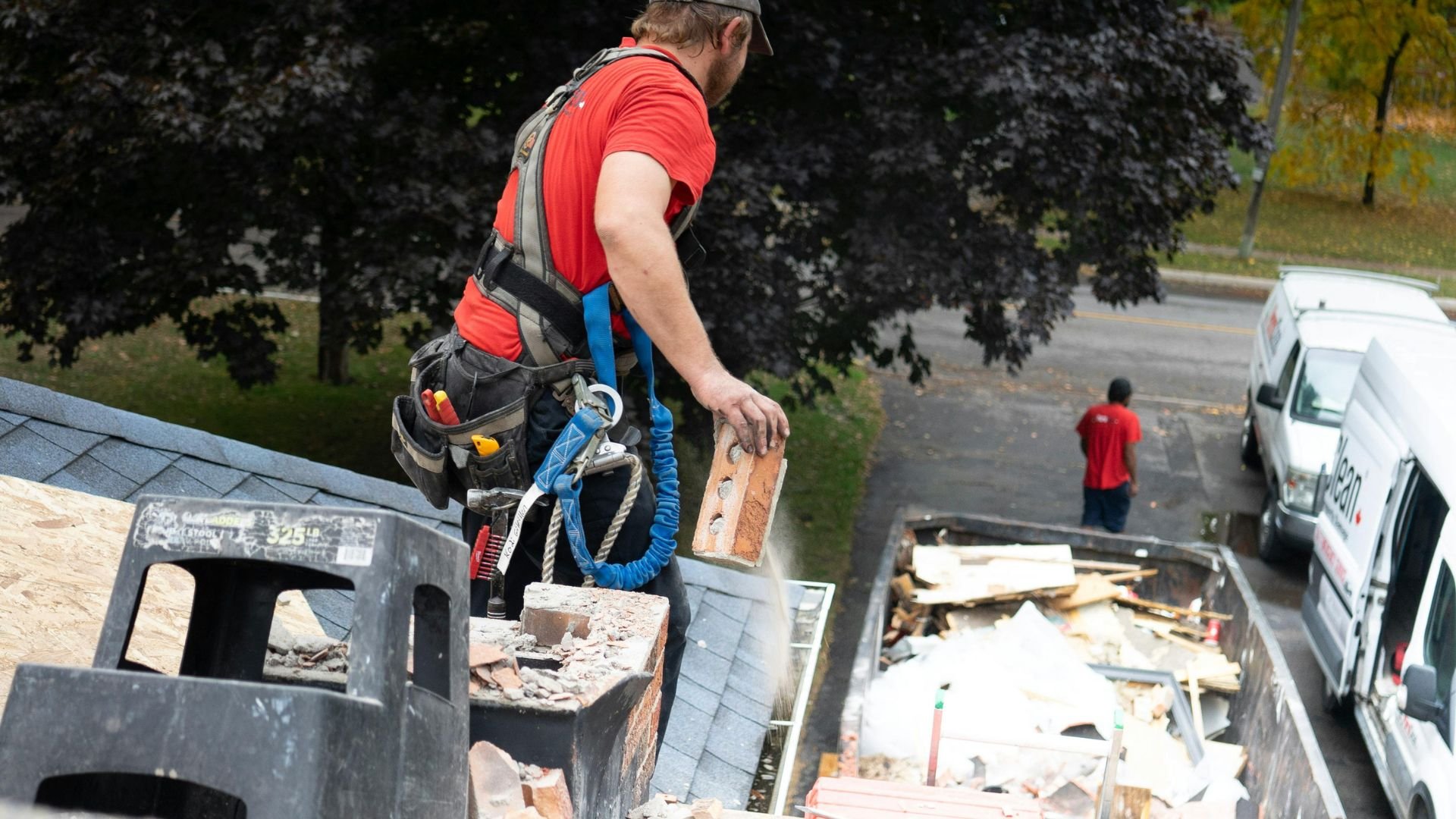Construction worker in safety harness removing debris from rooftop