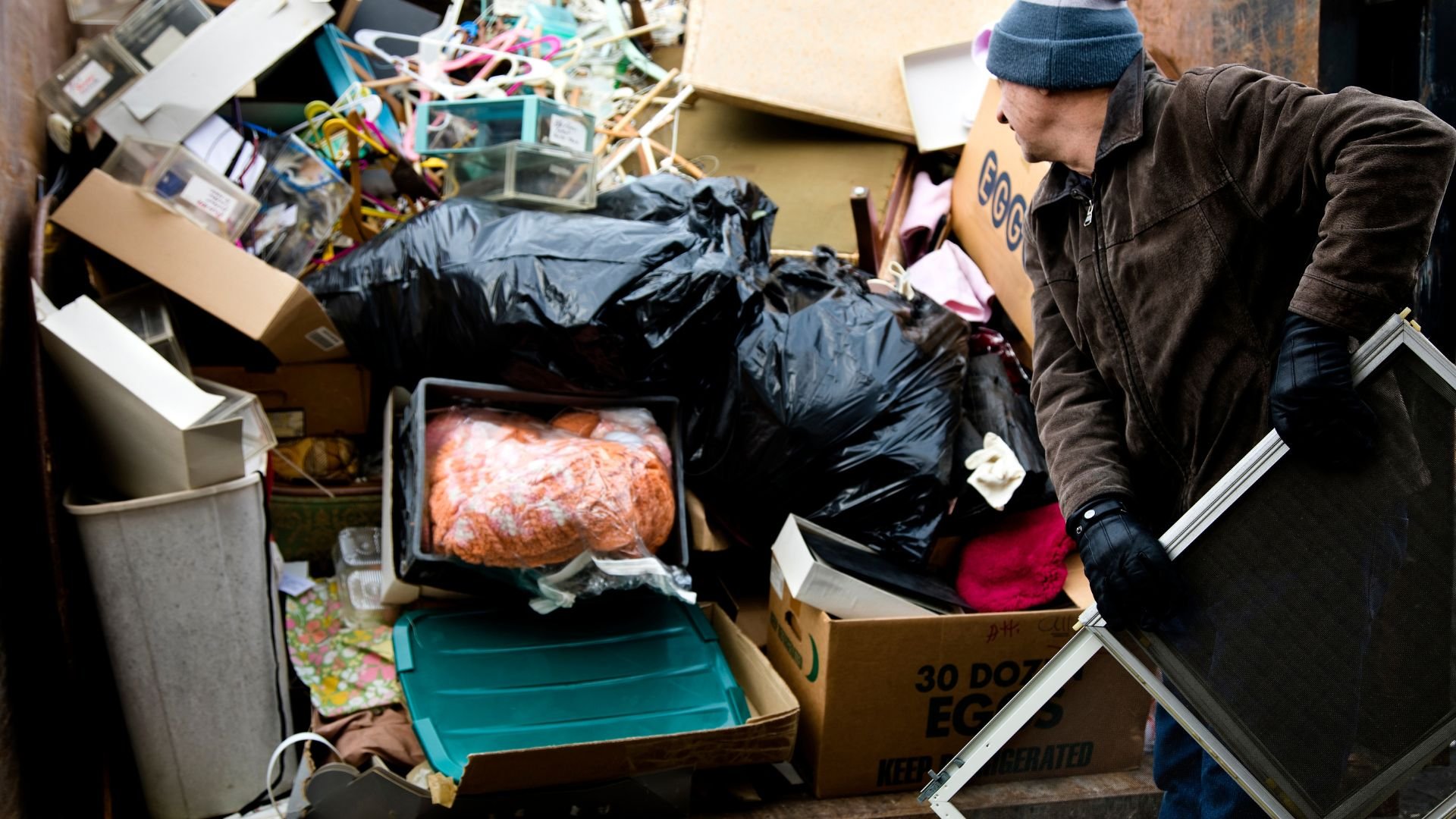 Cluttered storage area with trash bags, boxes, and a person sorting items