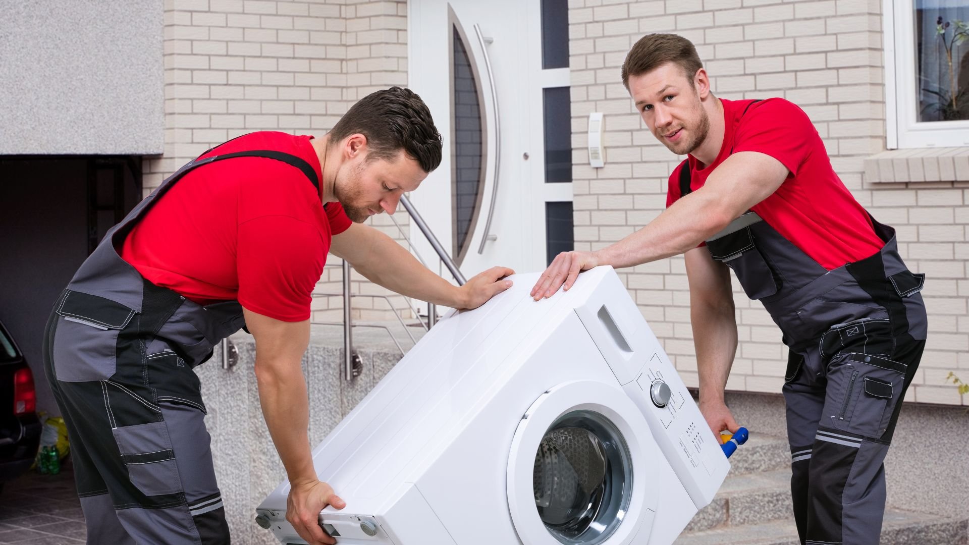 Two delivery workers carefully carrying a white washing machine outside