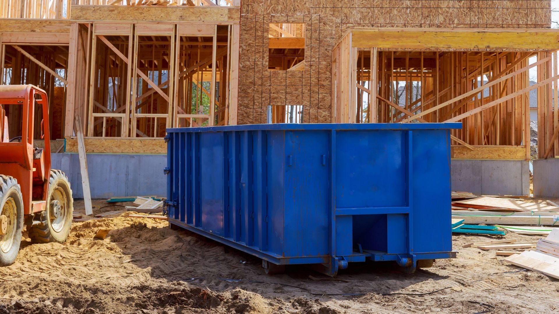 Large blue dumpster at residential construction site with wooden framing